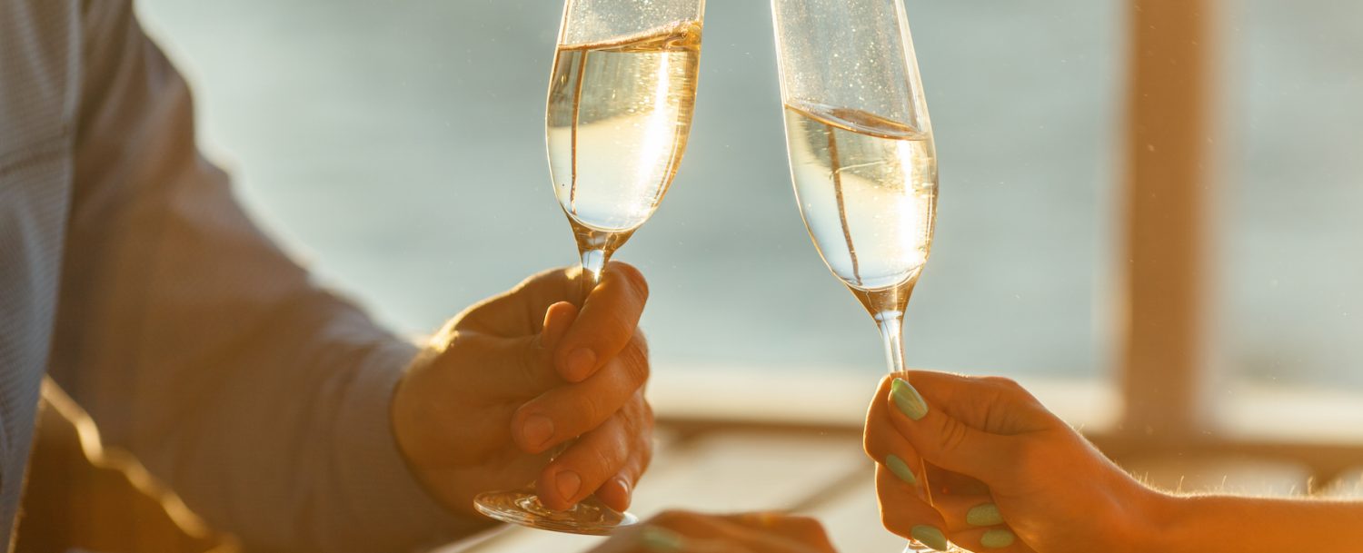 Man and woman holding champagne glasses with water view