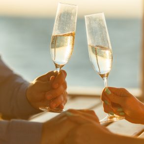 Man and woman holding champagne glasses with water view