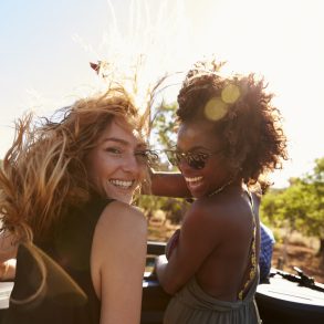 Two women standing in the back of open car turning to camera