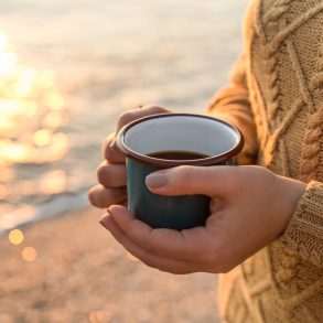Closeup shot of female hands in cozy sweater holding dark green mug with tea at sunset light with beautiful golden bokeh (Closeup shot of female hands in cozy sweater holding dark green mug with tea at sunset light with beautiful golden bokeh, ASCII,