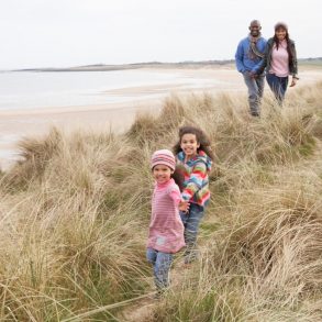 Family running along the beach in jackets.