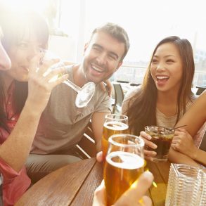 Group Of Friends Enjoying Drink At Outdoor Rooftop Bar Laughing And Chatting Around Table.