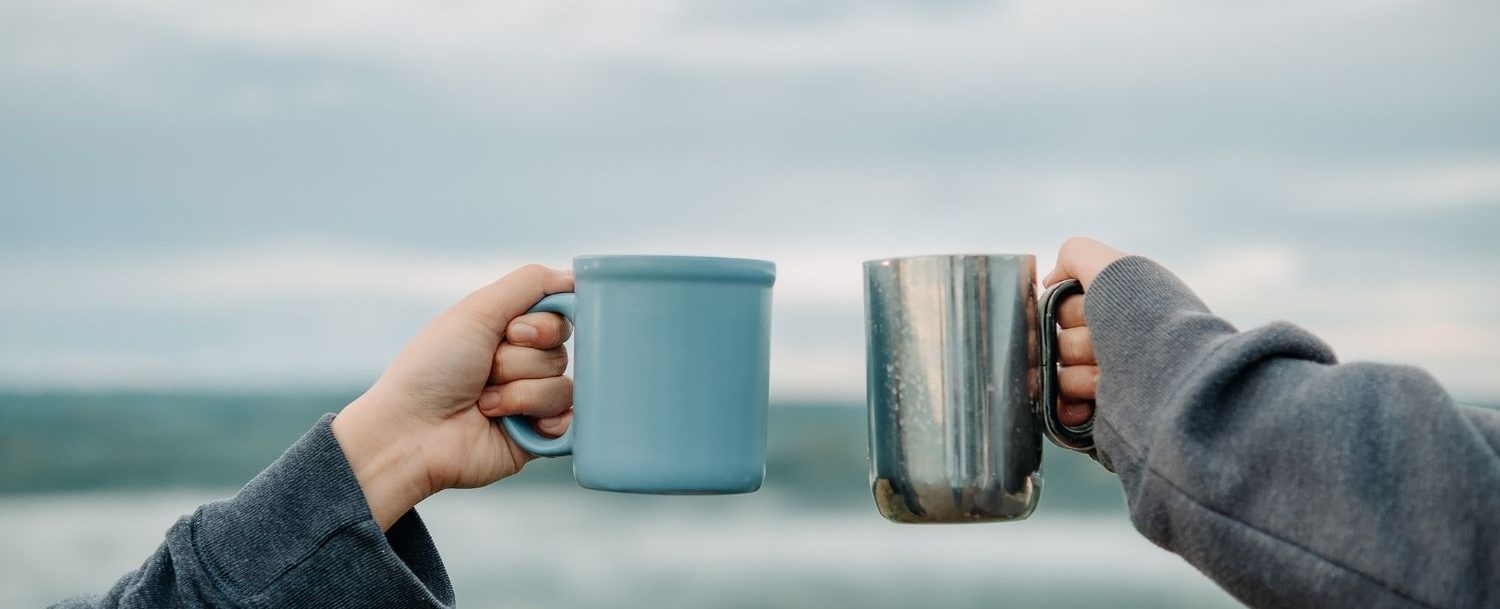 Two people holding coffee cups in front of the ocean.