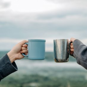 Two people holding coffee cups in front of the ocean.