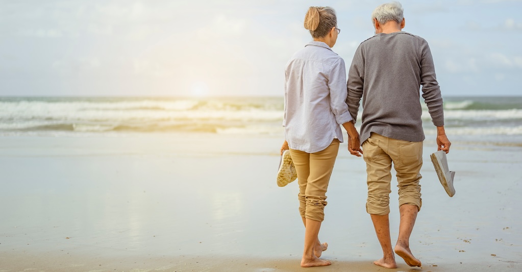 Senior couple walking on the beach and holding hands at sunrise.