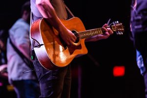 Musician playing acoustic guitar on stage during live concert.